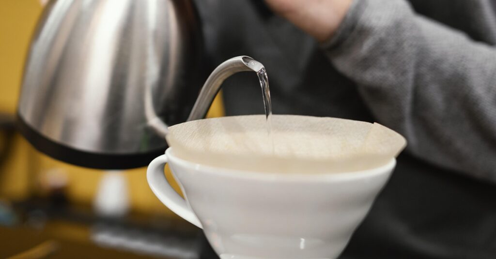 barista-masculino-com-avental-despejar-agua-no-filtro-de-cafe