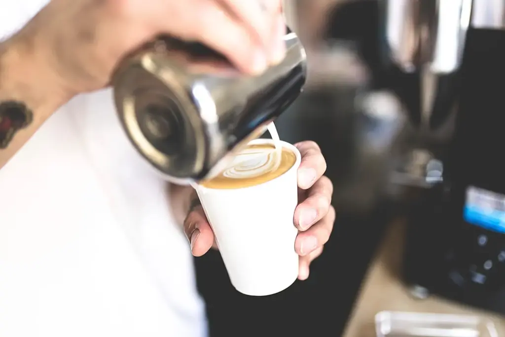 Leite sendo despejado numa xícara de café formando desenho na espuma