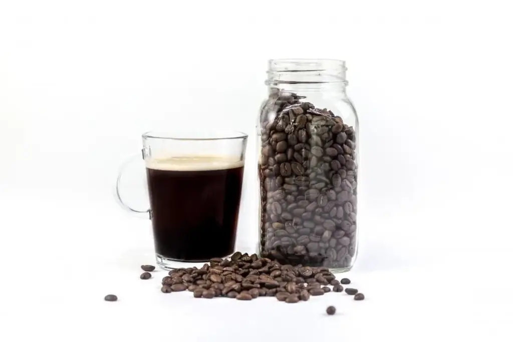 Grãos de café armazenados em pote de vidro ao lado de uma xícara