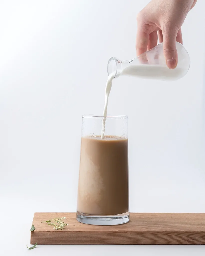 Leite sendo derramado num copo de café sobre tábua de madeira