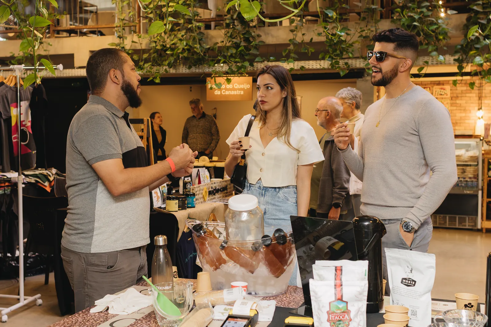 Expositor conversa com visitantes em estande de café com pacotes à mostra na feira